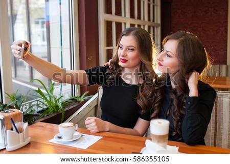 Two beautiful girls do selfi and drink coffee