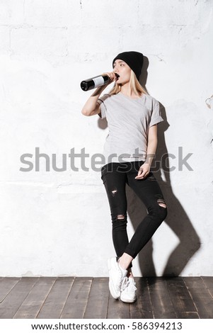Full length portrait of Hipster girl drinking wine from bottle