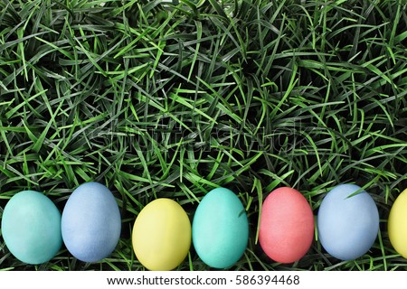 Overhead view of colorful Easter eggs lined up in a row over a background of grass. Flat lay style.