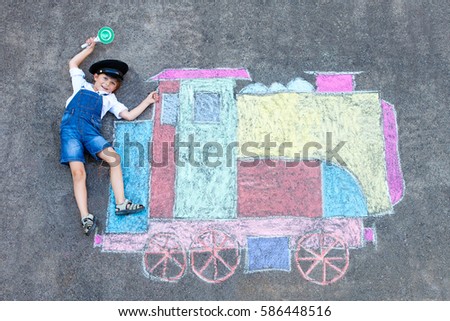 Happy little kid boy having fun with train or steam locomotive picture drawing with colorful chalks on ground. Children, lifestyle, fun concept. funny child playing and dreaming of profession.