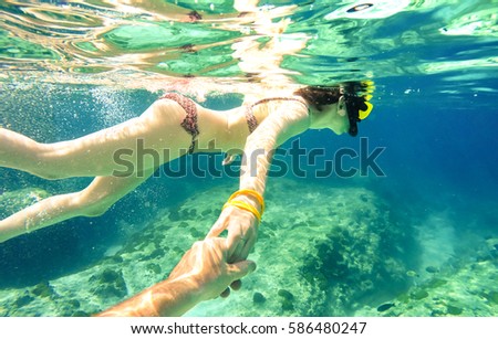 Snorkel couple swimming together in tropical sea with follow me composition - Snorkeling tour in exotic diving scenarios - Fun travel concept with active girl underwater - Soft focus due water density Royalty-Free Stock Photo #586480247
