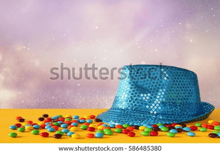 Blue shiny party Hat next to colorful candies on yellow wooden table