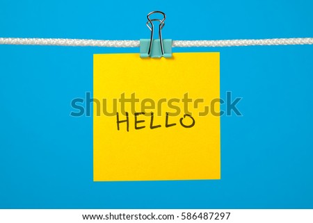 Yellow paper sheet on the string with text Hello over colorful background