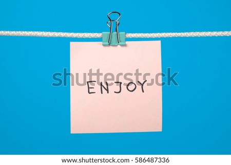 Pink paper note on clothesline with text Enjoy over colorful background