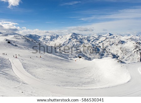 Skiers on a ski slope piste in winter alpine mountain resort with mountain range in background