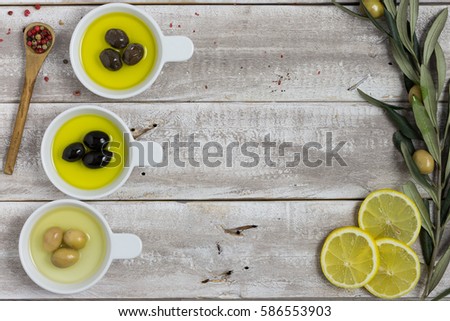 Green and black olives, olive oil in white round shaped bowls. Olive treen branches at the corners. Frame like composition with copy space.