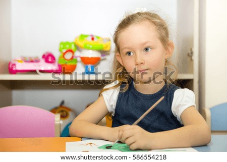 Adorable child girl draws a brush and paints in nursery room. Kid in kindergarten in Montessori preschool class.