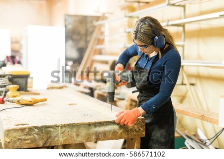 Young woman using a screwdriver on a piece of wood while working in a woodshop Royalty-Free Stock Photo #586571102