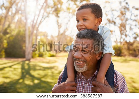 Grandfather Carries Grandson On Shoulders During Walk In Park Royalty-Free Stock Photo #586587587