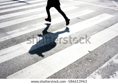 Blurry child's legs and kid's shadow with a backpack, on crossing while running over the street