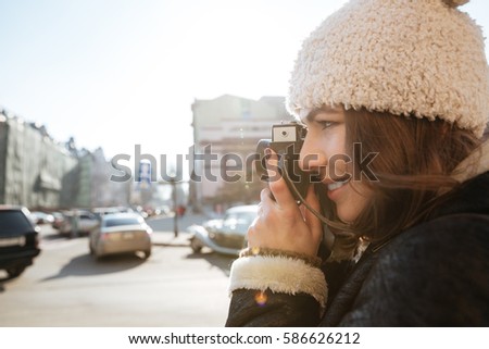 Picture of beautiful young woman photographer walking on the street wearing hat while holding camera.
