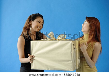 Two woman carrying big gift box, smiling at each other