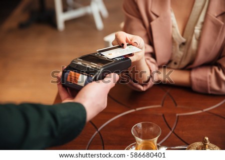Cropped photo of attractive young pretty woman sitting in cafe. Pays the order with credit card.