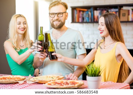 Young friends dressed casually in colorful t-shirts having having fun clinking bottles with beer and pizza at home