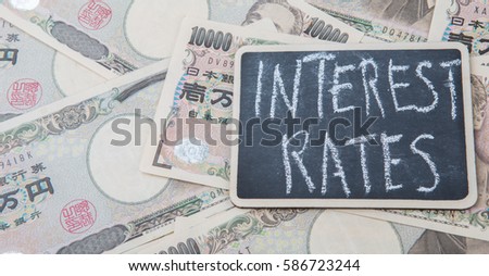 Concept image of Japan's Yen paper money with 'Interest Rates' written text on a mini blackboard.
