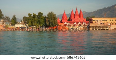 Reflection in water of bright red ancient temple and ghats at the Ganges river in Haridwar, India Royalty-Free Stock Photo #586743602