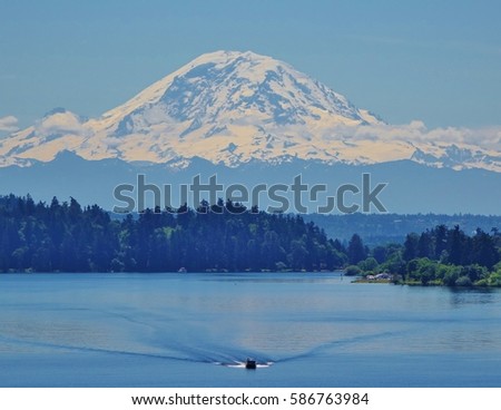 Lone boat on the water dwarfed by Mount Rainier 90 miles away. This view of the 14,410 foot mountain is from the Interstate 90 bridge that crosses Lake Washington in Seattle on a beautiful summer day.