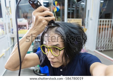 Man wearing glasses cutting his hair with razor 
