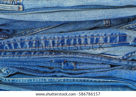 Stack of blue denim jeans background, close up. Double denim orange seam on bleached Denim jeans. 