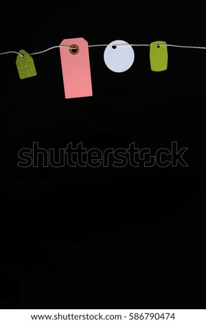 Colorful blank paper tags hanging on a string against black background. Copy space in lower part of vertical photo.