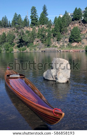 wooden strip built kayak on river with large rock
