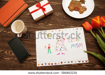 Happy mothers day card made by a child and a coffee cup on a wooden background of a table.