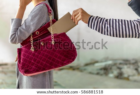 man pickpocketing a purse from woman's bag,selective focus on hand of pickpocket. Royalty-Free Stock Photo #586881518