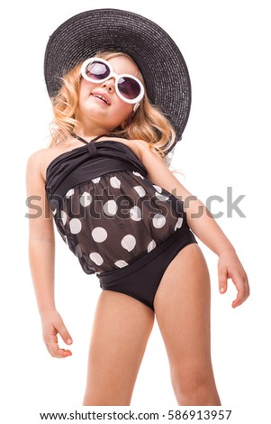 Isolated on white, cute pretty caucasian blonde girl in black swimwear, white sunglasses and big black hat stand, look at camera, turned head, laughing
Vertical picture