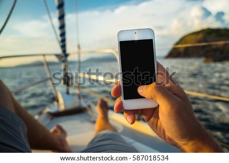 Rest on a yacht with a phone in hand. Summer leisure. Male lying on the deck and enjoy your smartphone. The guy doing the photo feet on the background seascape and yachts. Royalty-Free Stock Photo #587018534