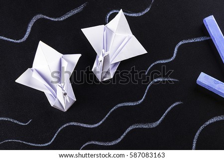 Two swans, origami, and blue chalk on dark background