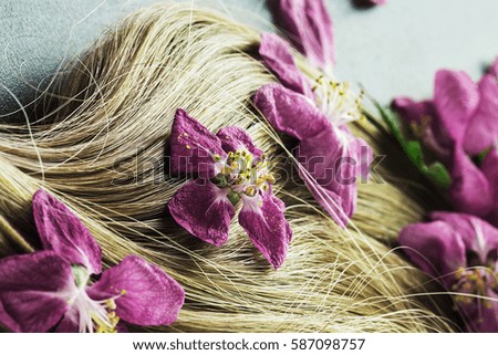 Beautiful, blond hair, decorated with fresh lilac flowers on a dark background closeup