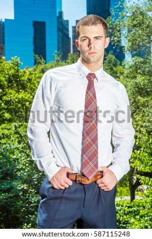 Portrait of Businessman in New York. Handsome professional guy wearing long sleeve white shirt, patterned tie, hands on belt, stands in font of business district, ready to work. Color filtered effect
