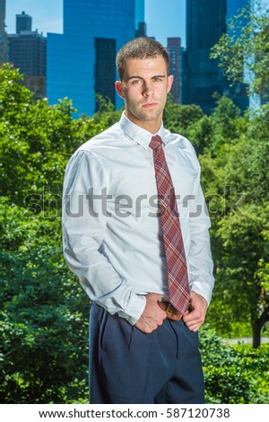 Portrait of Businessman in New York. Handsome professional guy wearing long sleeve white shirt, patterned tie, hands on belt, stands in font of business district, ready to work.
