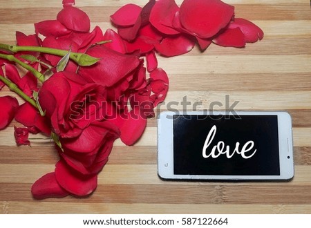 Red roses and smart phone on wooden table with word love