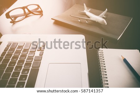 Business travel agency objects and equipment on computer working desk in vintage toning. Office desk with plane and computer for Business travel concept. Royalty-Free Stock Photo #587141357