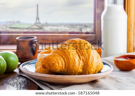 Delicious croissants with jam, milk, fresh fruits and milk for healthy breakfast. Traditional French meal on a table, Paris landscape behind a window on a background. French food tour.
