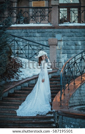 Beautiful lady in vintage white dress and a hat with feathers near her estate. Edwardian period wedding dress. 