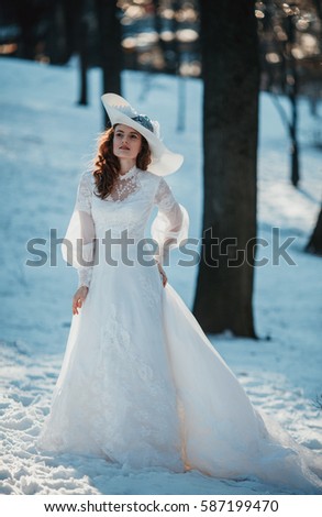 Beautiful lady in vintage white dress and a hat with feathers near her estate. Edwardian period wedding dress.