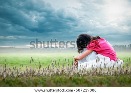 A little girl sitting in the grass on a sky bright with natural beauty.