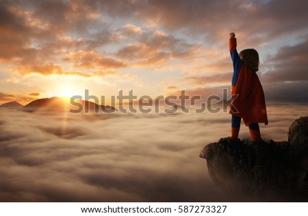 Little boy acting like a superhero on top of the mountain at sunset with copy space Royalty-Free Stock Photo #587273327