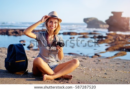 Sea vacation and hobby. Pretty young woman with camera and rucksack on the ocean beach.