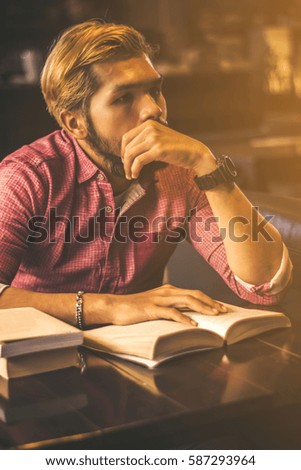 The blond man wearing a red shirt with long sleeves. Reading in coffee shop