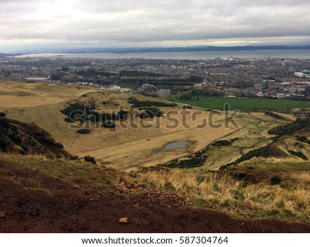 A picture of the Scottish countryside from atop a steep craggy hill with Edinburgh in the background