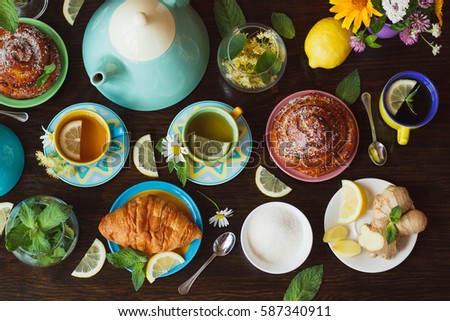 Cups of herbal tea with lemon and mint leaves, ginger root and croissant on the wooden background, top view