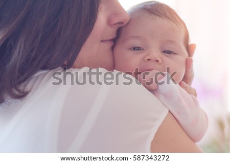 Mother with her newborn baby. Mother is holding her little baby girl.  Photo with the effect of sunlight, soft natural light, with selective focus. Baby on mom's shoulder.