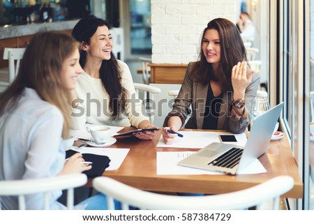Cheerful female editor of fashion magazine celebrating successful publication releasing in restaurant using laptop to read online feedback and reviews from readers greeting colleagues with achievement