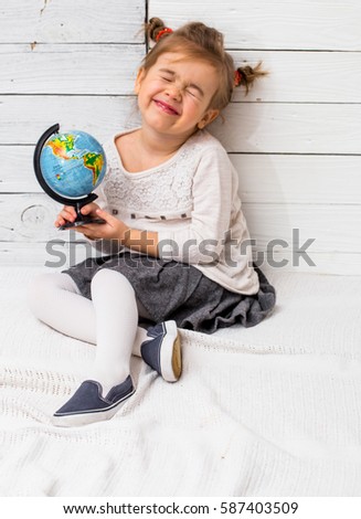 little cute girl sitting with a globe in hands on white wooden background ,concept of knowledge and travel