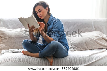 White cozy bed and a beautiful girl, reading a book, concepts of home and comfort, place for text Royalty-Free Stock Photo #587404685