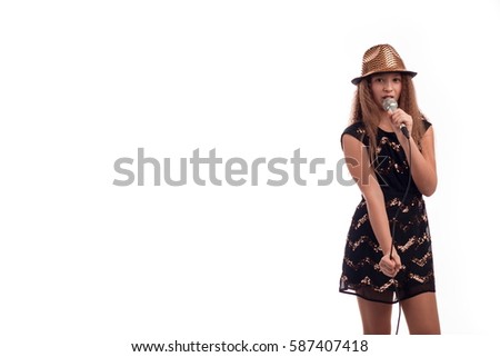 Young girl with long hair wearing a black dress and gold hat with a microphone on a white background in studio