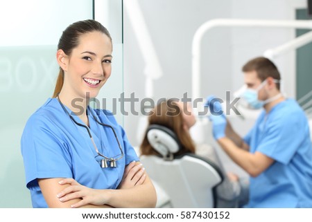 Dentist female with crossed arms wearing blue coat posing and looking at you at consultation with a doctor working with a patient in the background Royalty-Free Stock Photo #587430152